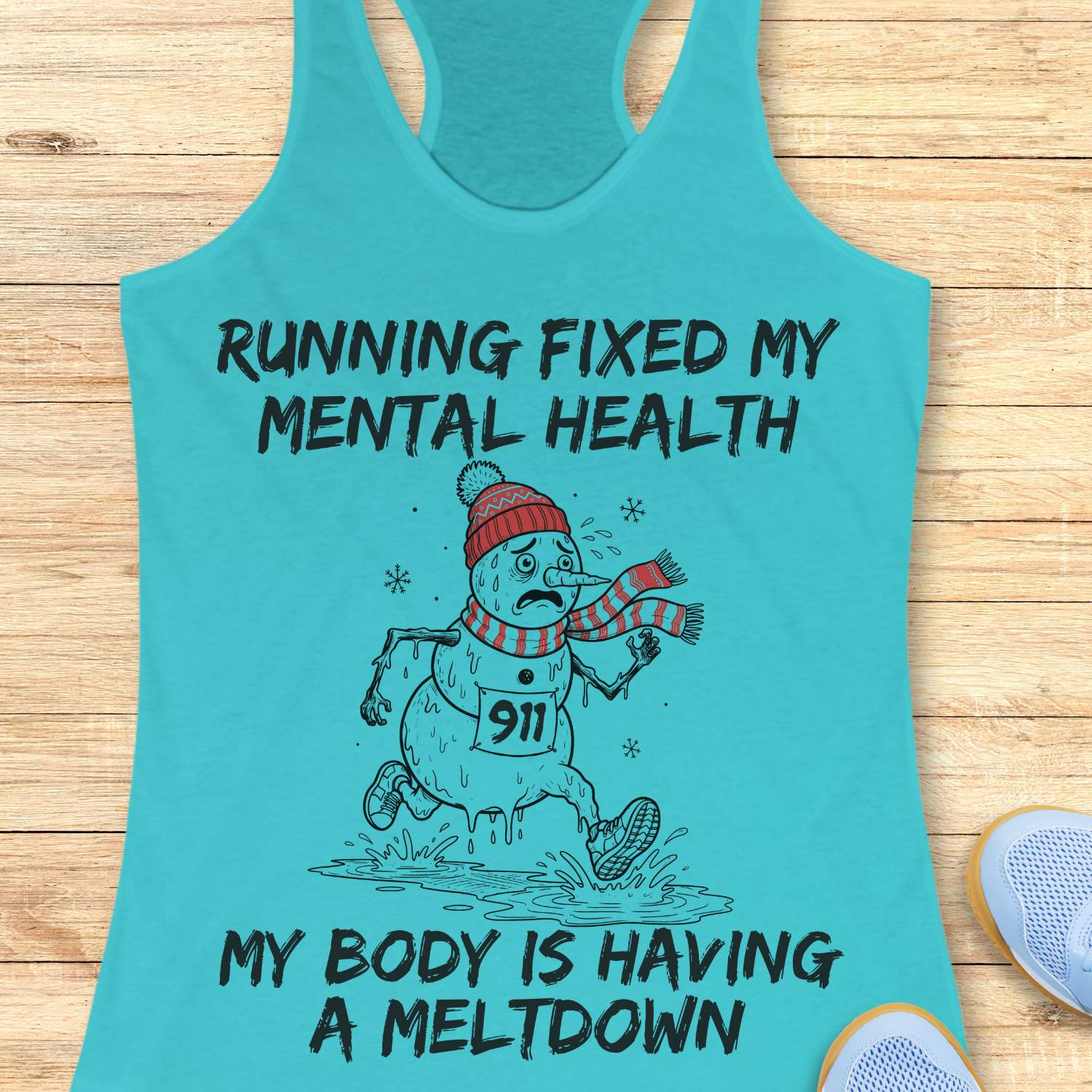 blue racerback tank top displayed on a light wooden surface featuring a humorous running-themed Christmas design. The graphic shows a melting snowman wearing a red knit hat, striped scarf, running shoes, and race bib number “911,” splashing through a puddle while running. Bold black text above and below the illustration reads: “RUNNING FIXED MY MENTAL HEALTH” and “MY BODY IS HAVING A MELTDOWN.” Partial blue athletic shoes are visible in the lower corners of the image.