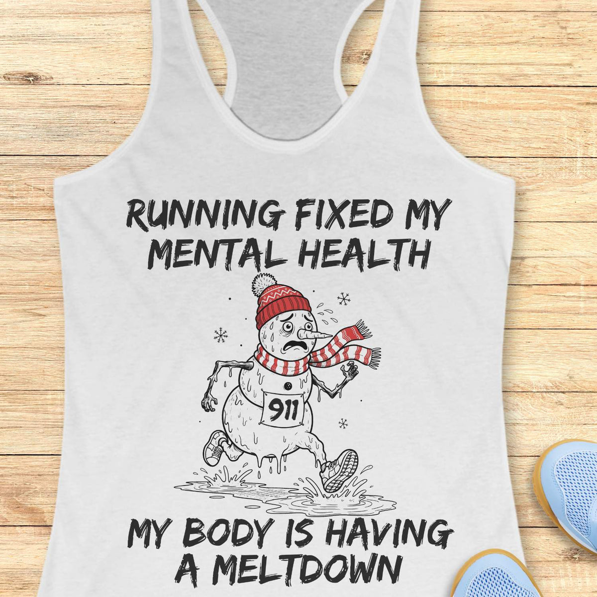 White racerback tank top displayed on a light wooden surface featuring a humorous running-themed Christmas design. The graphic shows a melting snowman wearing a red knit hat, striped scarf, running shoes, and race bib number “911,” splashing through a puddle while running. Bold black text above and below the illustration reads: “RUNNING FIXED MY MENTAL HEALTH” and “MY BODY IS HAVING A MELTDOWN.” Partial blue athletic shoes are visible in the lower corners of the image.