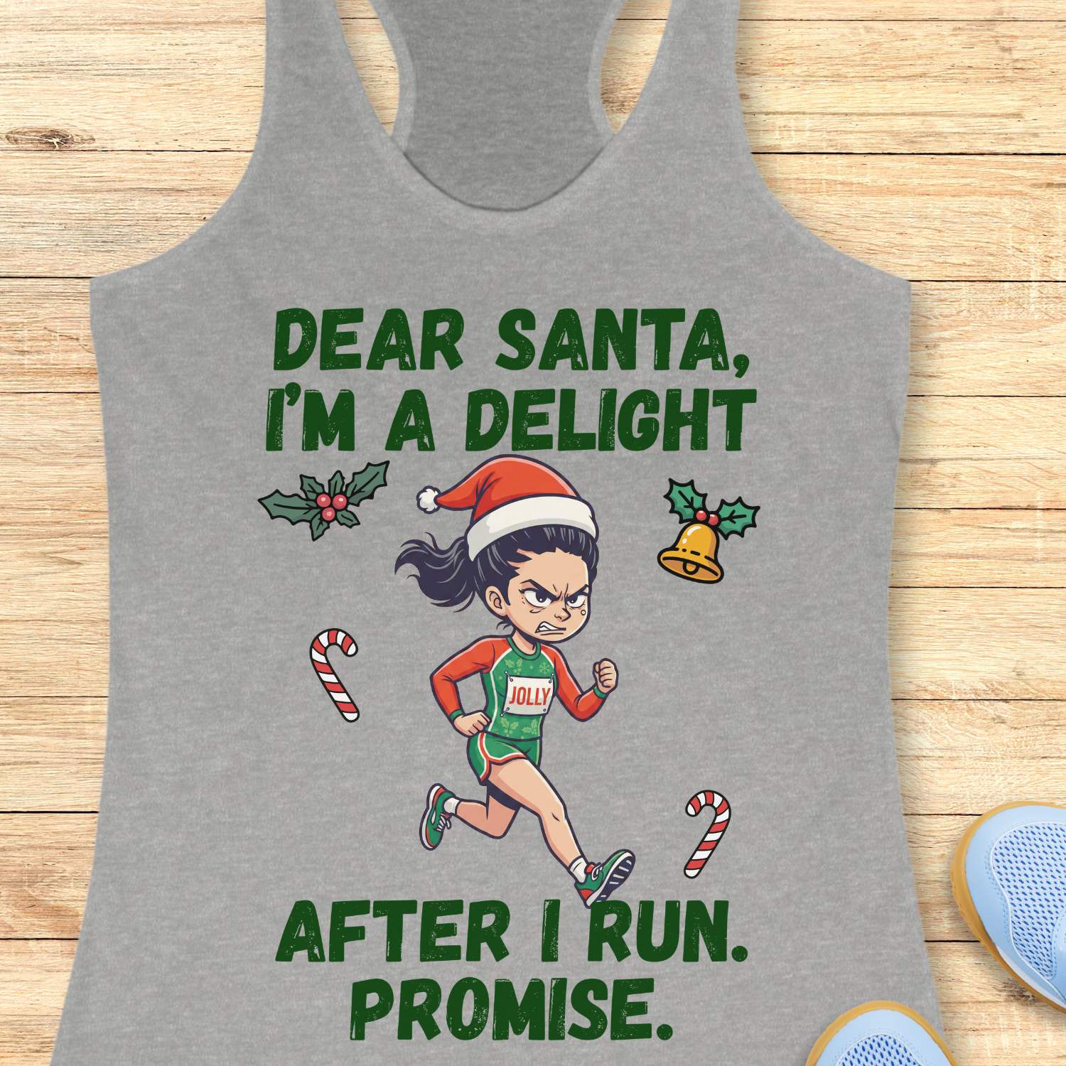 Heather gray racerback tank top displayed on a light wooden surface, featuring a festive running-themed graphic. The design shows a cartoon runner wearing a Santa hat, green running outfit with the word “JOLLY” on the chest, and running shoes. Holiday elements including holly leaves, a Christmas bell, and candy canes surround the runner. Bold green text above and below the illustration reads: “DEAR SANTA, I’M A DELIGHT” and “AFTER I RUN. PROMISE.” Partial blue athletic shoes are visible in the lower corners