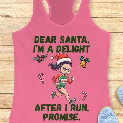 pink racerback tank top displayed on a light wooden surface, featuring a festive running-themed graphic. The design shows a cartoon runner wearing a Santa hat, green running outfit with the word “JOLLY” on the chest, and running shoes. Holiday elements including holly leaves, a Christmas bell, and candy canes surround the runner. Bold green text above and below the illustration reads: “DEAR SANTA, I’M A DELIGHT” and “AFTER I RUN. PROMISE.” Partial blue athletic shoes are visible in the lower corners