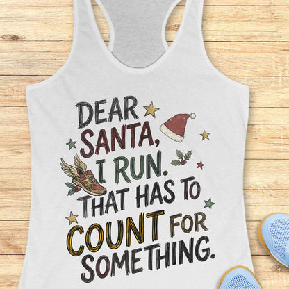 white racerback tank top displayed on a light wooden surface, featuring a festive running-themed typographic design. The graphic includes the humorous text: “DEAR SANTA, I RUN. THAT HAS TO COUNT FOR SOMETHING.” Decorative holiday elements surround the text, including a red Santa hat, a winged running shoe, holly sprigs with berries, and colorful stars. The word “COUNT” is highlighted in yellow, while the remaining text appears in black. Partial blue athletic shoes are visible in the lower corners, rei