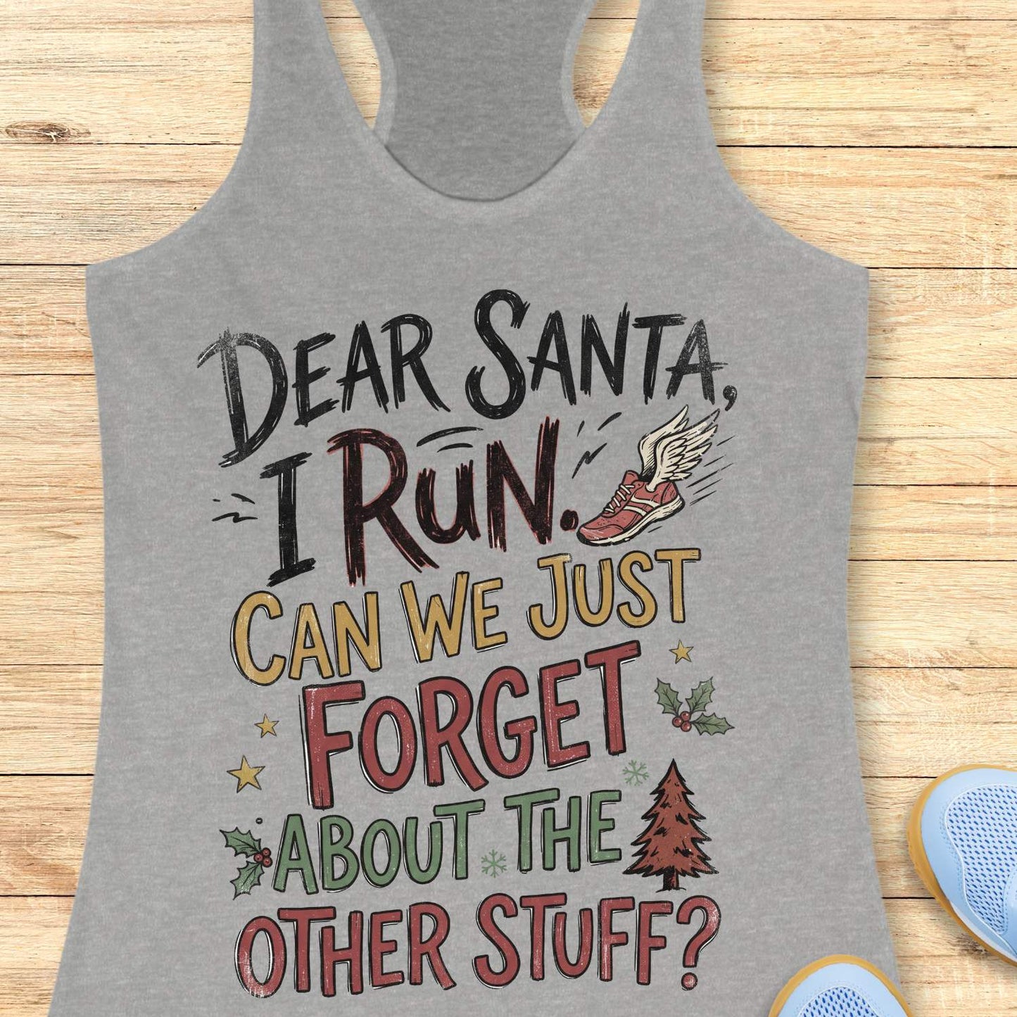 grey racerback tank top displayed on a light wooden surface, featuring a festive running-themed typography design. The graphic includes the humorous text: “DEAR SANTA, I RUN. CAN WE JUST FORGET ABOUT THE OTHER STUFF?” Decorative holiday accents surround the text, including a winged running shoe, holly sprigs with red berries, gold stars, snowflakes, and a Christmas tree. The design uses black, red, green, and gold lettering for a playful holiday look. Partial blue athletic shoes are visible in the lower co