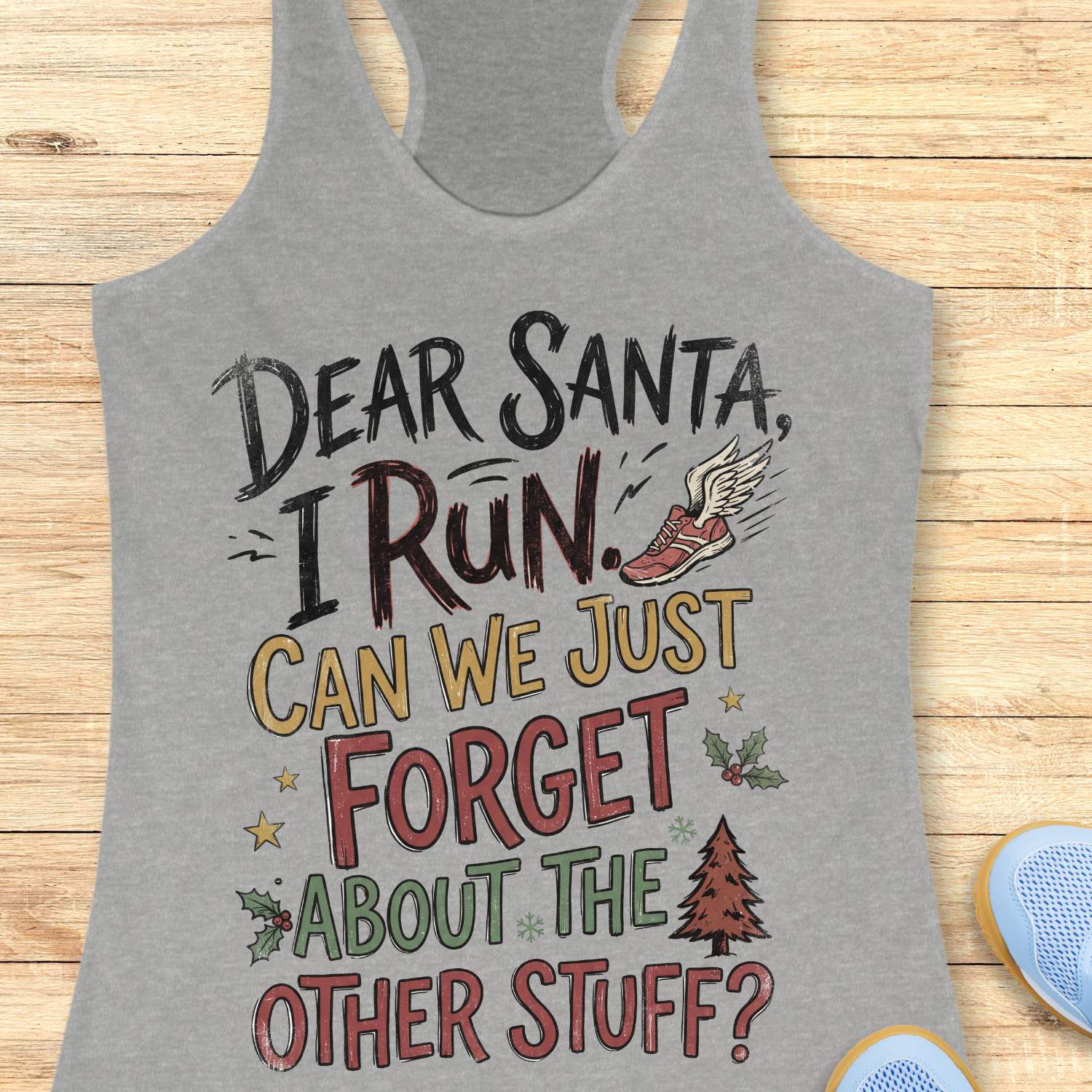 grey racerback tank top displayed on a light wooden surface, featuring a festive running-themed typography design. The graphic includes the humorous text: “DEAR SANTA, I RUN. CAN WE JUST FORGET ABOUT THE OTHER STUFF?” Decorative holiday accents surround the text, including a winged running shoe, holly sprigs with red berries, gold stars, snowflakes, and a Christmas tree. The design uses black, red, green, and gold lettering for a playful holiday look. Partial blue athletic shoes are visible in the lower co