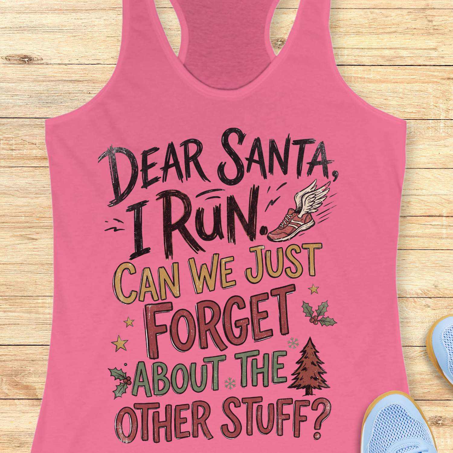 pink racerback tank top displayed on a light wooden surface, featuring a festive running-themed typography design. The graphic includes the humorous text: “DEAR SANTA, I RUN. CAN WE JUST FORGET ABOUT THE OTHER STUFF?” Decorative holiday accents surround the text, including a winged running shoe, holly sprigs with red berries, gold stars, snowflakes, and a Christmas tree. The design uses black, red, green, and gold lettering for a playful holiday look. Partial blue athletic shoes are visible in the lower co