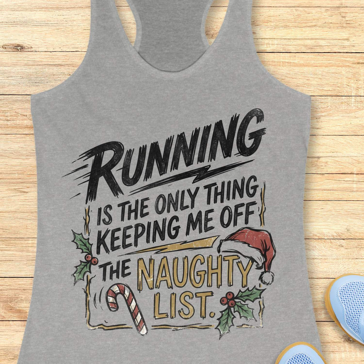 grey racerback tank top displayed on a light wooden surface, featuring a festive running-themed typography design. The graphic displays the humorous text: “RUNNING IS THE ONLY THING KEEPING ME OFF THE NAUGHTY LIST.” Holiday decorations include a red Santa hat, holly sprigs with red berries, a striped candy cane, and accent graphics surrounding the text. The words “NAUGHTY LIST” are highlighted in gold, while the remaining text appears in black. Partial blue athletic shoes are visible in the lower corn