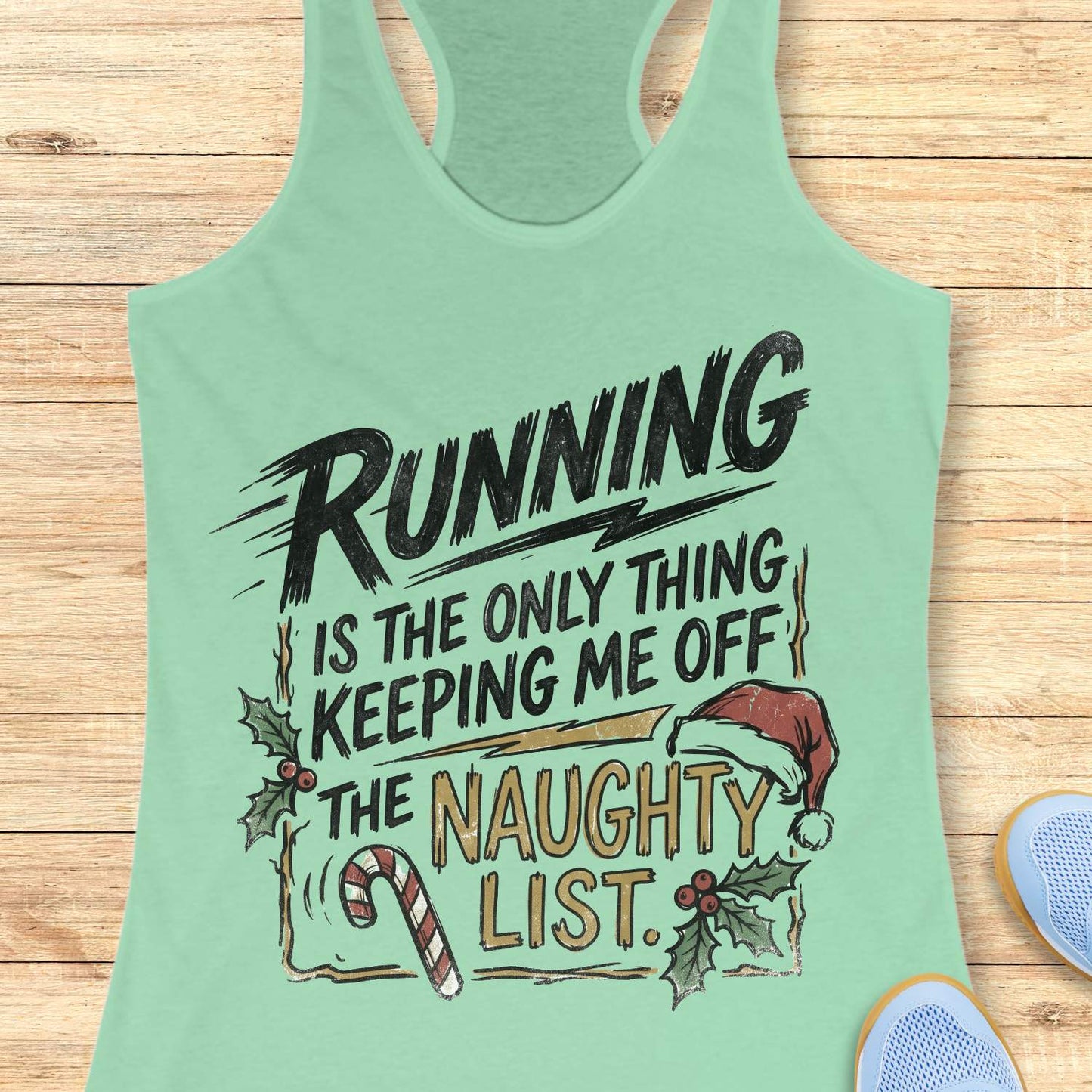 Mint green racerback tank top displayed on a light wooden surface, featuring a festive running-themed typography design. The graphic displays the humorous text: “RUNNING IS THE ONLY THING KEEPING ME OFF THE NAUGHTY LIST.” Holiday decorations include a red Santa hat, holly sprigs with red berries, a striped candy cane, and accent graphics surrounding the text. The words “NAUGHTY LIST” are highlighted in gold, while the remaining text appears in black. Partial blue athletic shoes are visible in the lower corn