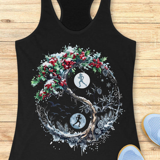 Black racerback tank top displayed on a light wooden surface, featuring an intricate winter-themed circular tree design inspired by a yin-yang composition. The artwork shows a twisting tree with one side covered in green holly leaves and bright red berries dusted with snow, while the opposite side features frosted branches, pinecones, and winter foliage. Two silhouetted runners appear within glowing moon-like circles positioned opposite each other inside the design. Snowflakes, birds in flight, swirling dec