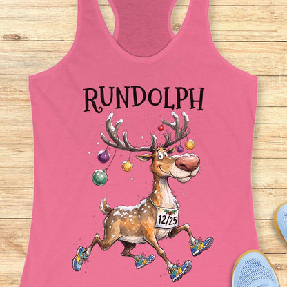 pink racerback tank top featuring the word “RUNDOLPH” above a playful cartoon reindeer running in colorful athletic shoes. The reindeer has snow-dusted antlers decorated with hanging Christmas ornaments and wears a race bib displaying “12/25.” Snowflakes are scattered throughout the design, adding a festive winter feel. The humorous artwork combines holiday cheer and running culture, making it perfect for runners who love Christmas-themed race apparel.