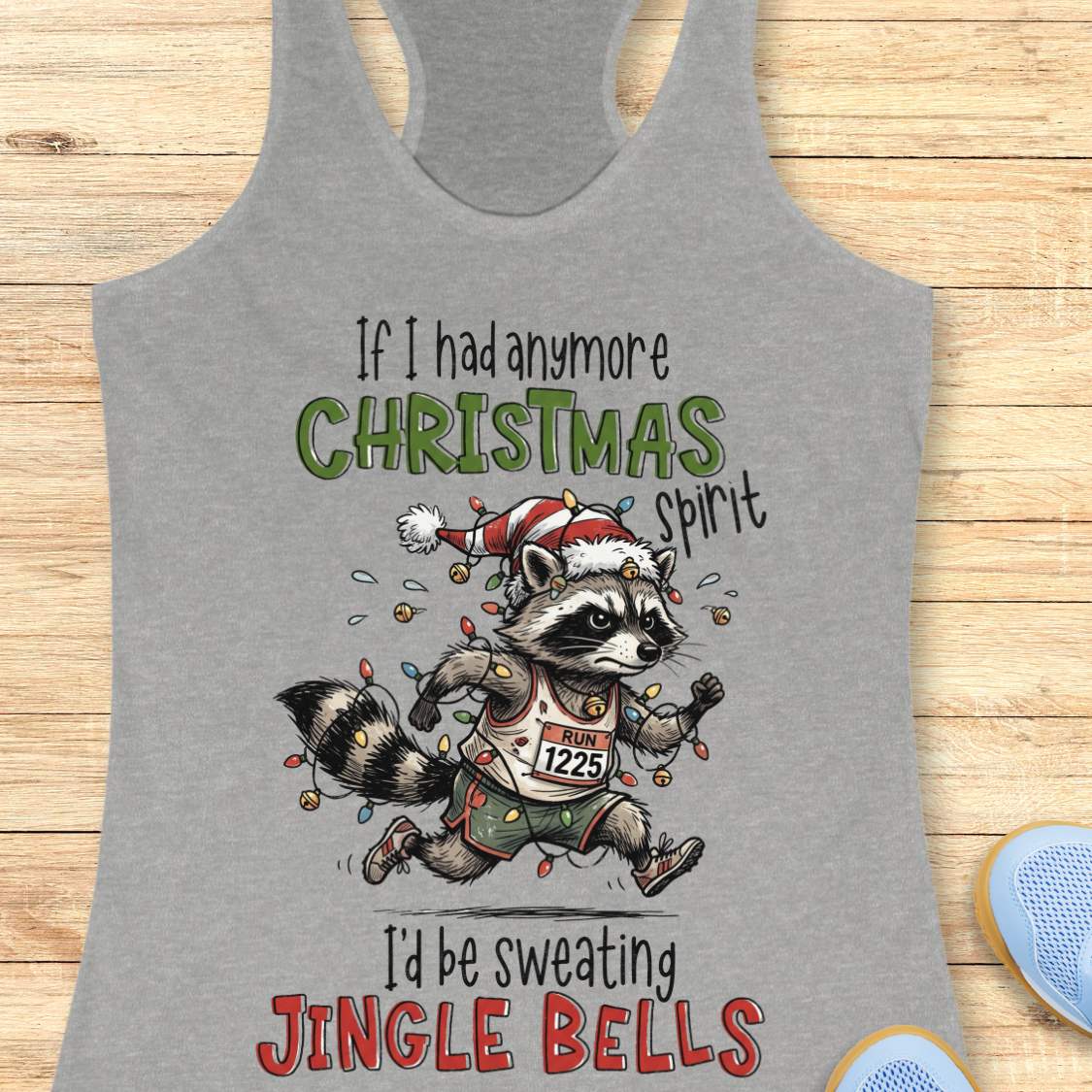 grey racerback tank top featuring the humorous Christmas running quote “If I had anymore Christmas spirit I’d be sweating Jingle Bells.” The design shows a cartoon raccoon runner wearing a Santa hat and wrapped in colorful Christmas lights while running in athletic gear. The raccoon wears a race bib labeled “RUN 1225” and is surrounded by festive holiday lights and jingle bells. The playful artwork combines Christmas cheer, running humor, and woodland charm, making it perfect for runners who love holiday r