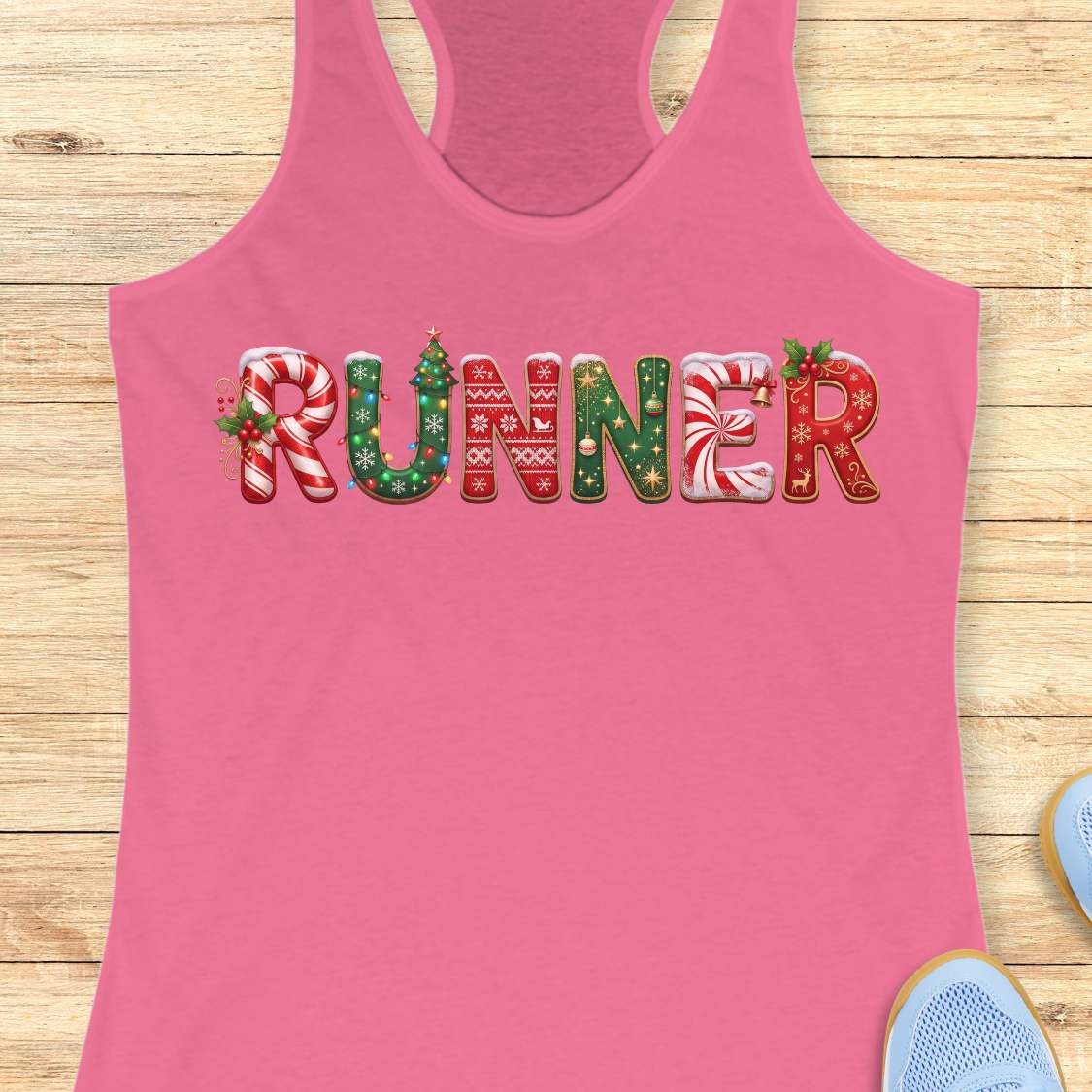 pink racerback tank top featuring the word “RUNNER” in large festive Christmas-themed letters. The letters are decorated with candy cane stripes, holiday sweater patterns, ornaments, holly leaves, bells, snowflakes, and Christmas tree designs in red, green, and white. The tank top is displayed on a light wood background with partial blue running shoes visible in the corners.