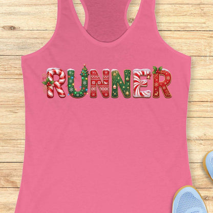 pink racerback tank top featuring the word “RUNNER” in large festive Christmas-themed letters. The letters are decorated with candy cane stripes, holiday sweater patterns, ornaments, holly leaves, bells, snowflakes, and Christmas tree designs in red, green, and white. The tank top is displayed on a light wood background with partial blue running shoes visible in the corners.
