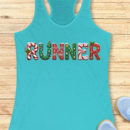 blue racerback tank top featuring the word “RUNNER” in large festive Christmas-themed letters. The letters are decorated with candy cane stripes, holiday sweater patterns, ornaments, holly leaves, bells, snowflakes, and Christmas tree designs in red, green, and white. The tank top is displayed on a light wood background with partial blue running shoes visible in the corners.
