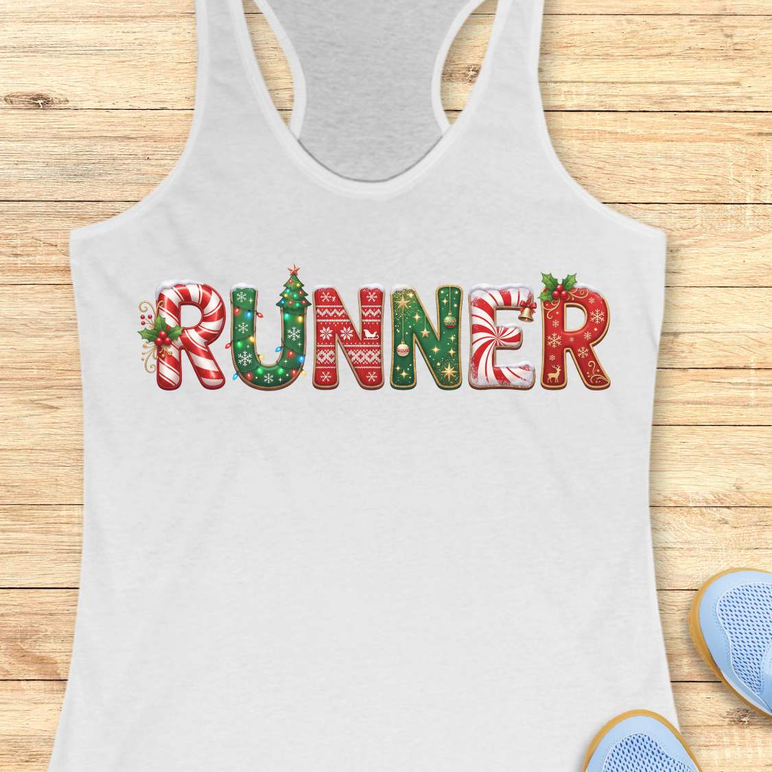 White racerback tank top featuring the word “RUNNER” in large festive Christmas-themed letters. The letters are decorated with candy cane stripes, holiday sweater patterns, ornaments, holly leaves, bells, snowflakes, and Christmas tree designs in red, green, and white. The tank top is displayed on a light wood background with partial blue running shoes visible in the corners.