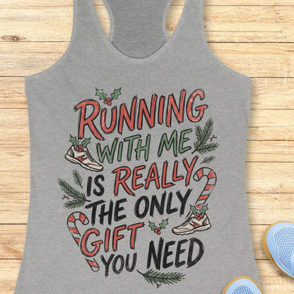 A heather gray racerback tank top with a festive Christmas-themed graphic reading 'RUNNING WITH ME IS REALLY THE ONLY GIFT YOU NEED' in red, green, and black lettering, styled flat on a light wood background.