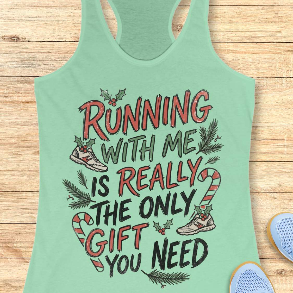 mint racerback tank top featuring the festive running-themed phrase “RUNNING WITH ME IS REALLY THE ONLY GIFT YOU NEED” in large red, green, and black hand-lettered text. The design is decorated with candy canes, holly leaves and berries, evergreen branches, and running shoes accented with holiday greenery. The playful Christmas artwork combines holiday cheer with a runner’s sense of humor. The tank top is displayed on a light wood background with partial blue running shoes visible in the corners.