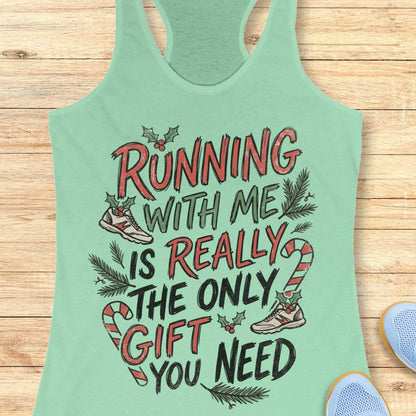 mint racerback tank top featuring the festive running-themed phrase “RUNNING WITH ME IS REALLY THE ONLY GIFT YOU NEED” in large red, green, and black hand-lettered text. The design is decorated with candy canes, holly leaves and berries, evergreen branches, and running shoes accented with holiday greenery. The playful Christmas artwork combines holiday cheer with a runner’s sense of humor. The tank top is displayed on a light wood background with partial blue running shoes visible in the corners.