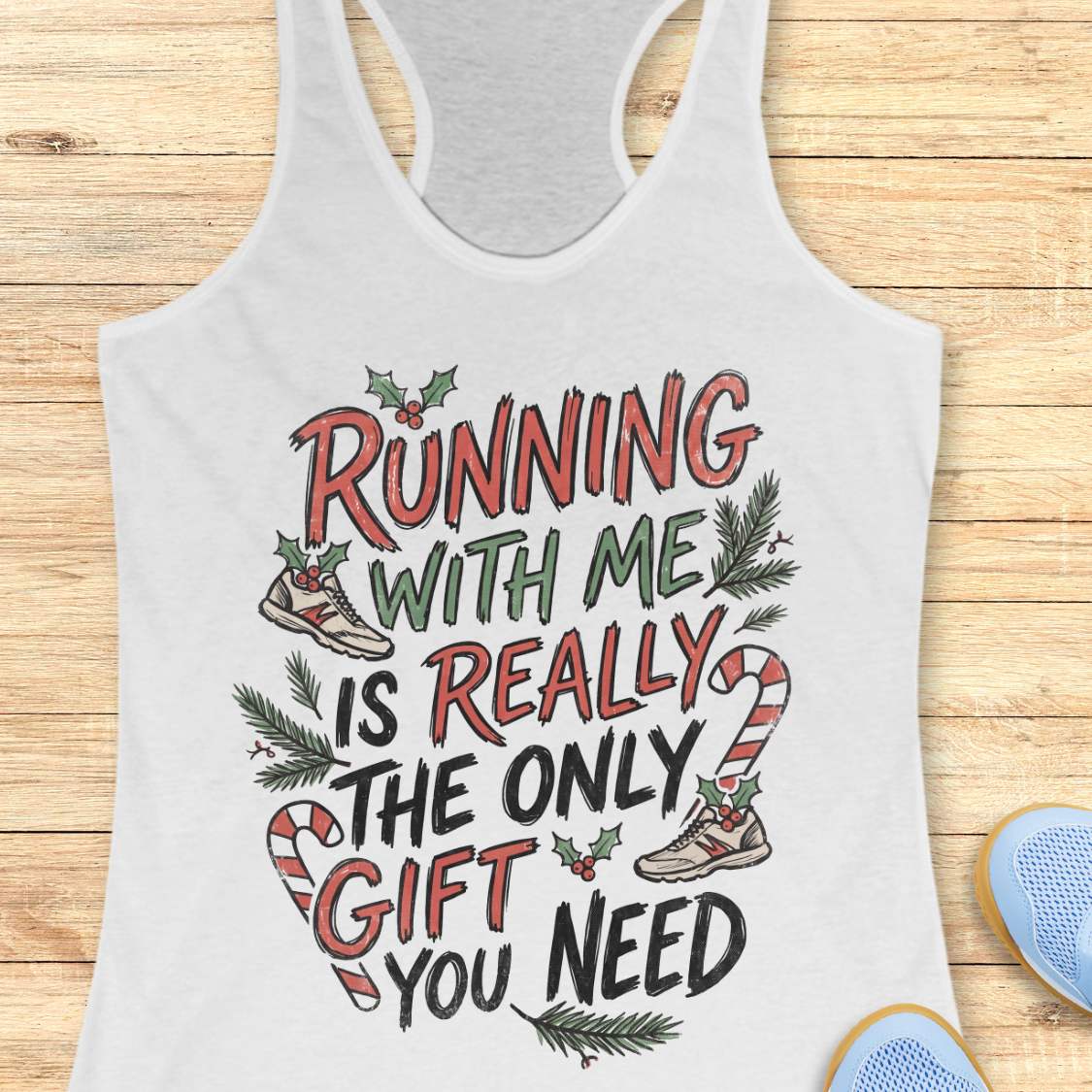 white racerback tank top featuring the festive running-themed phrase “RUNNING WITH ME IS REALLY THE ONLY GIFT YOU NEED” in large red, green, and black hand-lettered text. The design is decorated with candy canes, holly leaves and berries, evergreen branches, and running shoes accented with holiday greenery. The playful Christmas artwork combines holiday cheer with a runner’s sense of humor. The tank top is displayed on a light wood background with partial blue running shoes visible in the corners.
