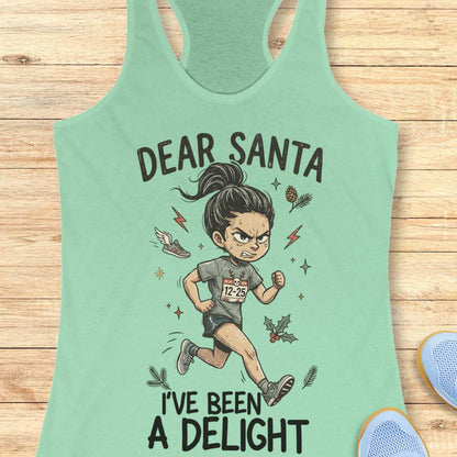 Mint green racerback tank top featuring the humorous Christmas running phrase “DEAR SANTA I’VE BEEN A DELIGHT” in bold black lettering. The design includes a cartoon runner wearing a race bib marked “12-25,” surrounded by holiday accents such as holly leaves, pine sprigs, stars, and a winged running shoe. The festive artwork combines runner humor with Christmas cheer. The tank top is displayed on a light wood background with partial blue running shoes visible in the corners.