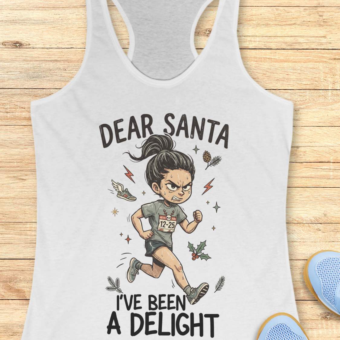 A white racerback tank top laid flat on a light wood background, featuring a cartoon illustration of a woman running with the text 'DEAR SANTA I'VE BEEN A DELIGHT'. Partial blue shoes are visible at the bottom right as styling props.