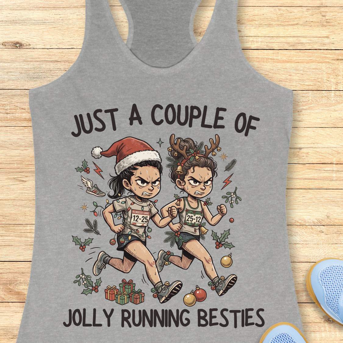 grey racerback running tank top displayed on a wooden background featuring a festive illustration of two runners in holiday outfits. One runner wears a Santa hat and the other wears reindeer antlers adorned with Christmas decorations. The runners are dressed in race gear, surrounded by holly, ornaments, presents, and holiday accents. The design includes the text: “JUST A COUPLE OF JOLLY RUNNING BESTIES.” Blue running shoes are partially visible at the bottom corners of the image.