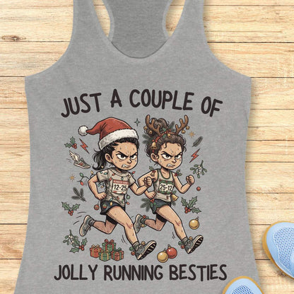 grey racerback running tank top displayed on a wooden background featuring a festive illustration of two runners in holiday outfits. One runner wears a Santa hat and the other wears reindeer antlers adorned with Christmas decorations. The runners are dressed in race gear, surrounded by holly, ornaments, presents, and holiday accents. The design includes the text: “JUST A COUPLE OF JOLLY RUNNING BESTIES.” Blue running shoes are partially visible at the bottom corners of the image.
