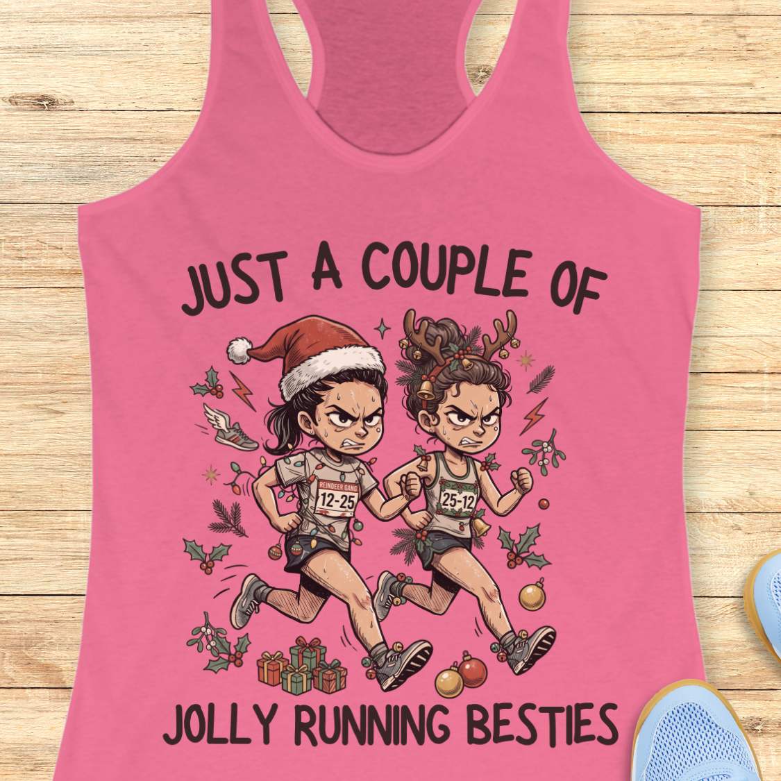 pink racerback running tank top displayed on a wooden background featuring a festive illustration of two runners in holiday outfits. One runner wears a Santa hat and the other wears reindeer antlers adorned with Christmas decorations. The runners are dressed in race gear, surrounded by holly, ornaments, presents, and holiday accents. The design includes the text: “JUST A COUPLE OF JOLLY RUNNING BESTIES.” Blue running shoes are partially visible at the bottom corners of the image.