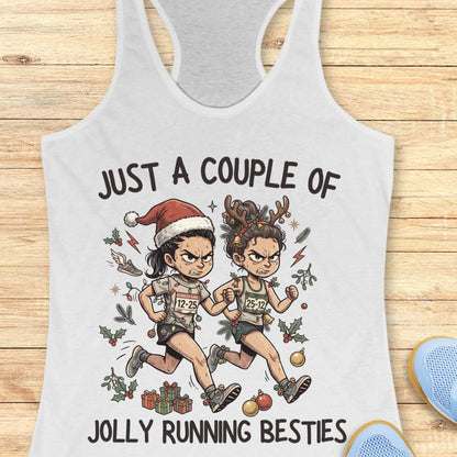 White racerback running tank top displayed on a wooden background featuring a festive illustration of two runners in holiday outfits. One runner wears a Santa hat and the other wears reindeer antlers adorned with Christmas decorations. The runners are dressed in race gear, surrounded by holly, ornaments, presents, and holiday accents. The design includes the text: “JUST A COUPLE OF JOLLY RUNNING BESTIES.” Blue running shoes are partially visible at the bottom corners of the image.