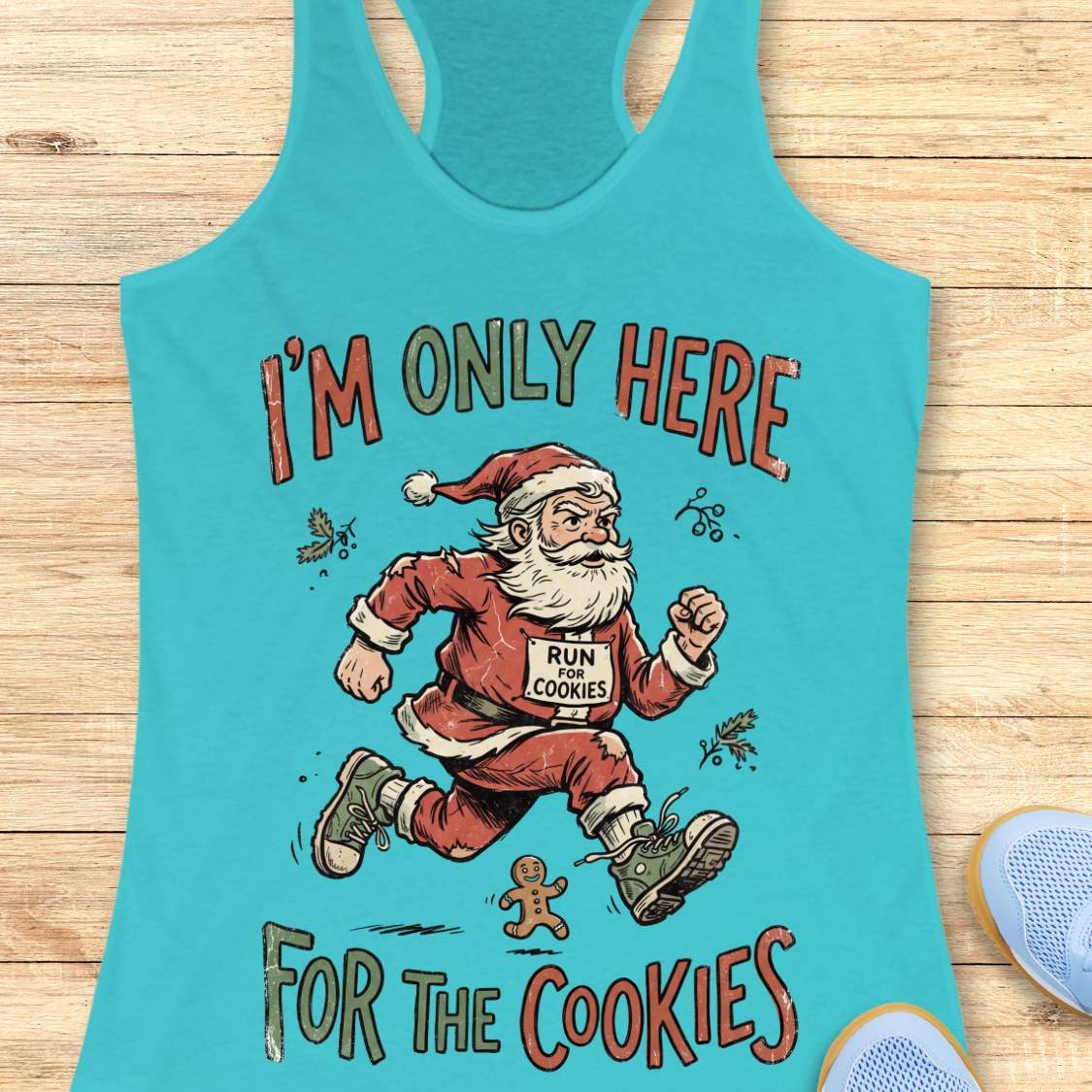 A turquoise racerback tank top laid flat on a light wood surface, featuring a festive graphic of Santa Claus running with a sign that reads 'RUN FOR COOKIES' and the text 'I'M ONLY HERE FOR THE COOKIES' in red and green lettering.