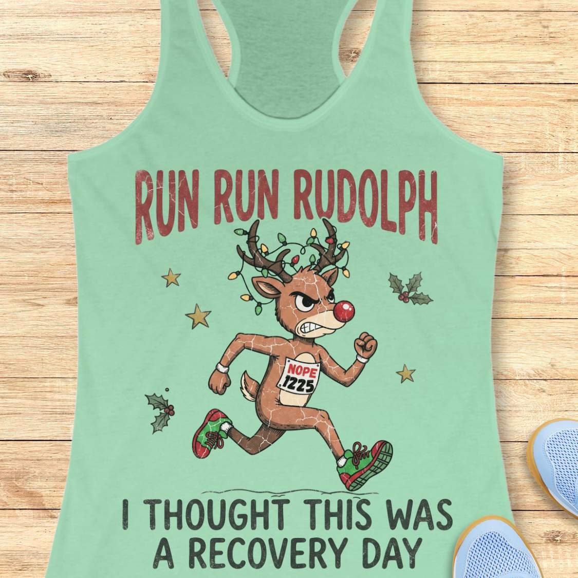 Funny Christmas runner tank top featuring Rudolph the Red-Nosed Reindeer dressed as a runner, sprinting in red and green running shoes with a race bib that reads "NOPE 1225." Rudolph's antlers are wrapped in colorful Christmas lights, and festive holly leaves and stars surround the character. Large distressed text reads, "RUN RUN RUDOLPH" above the illustration and "I THOUGHT THIS WAS A RECOVERY DAY" below. The design is printed on a mint green racerback tank top and combines holiday humor with a relatable 