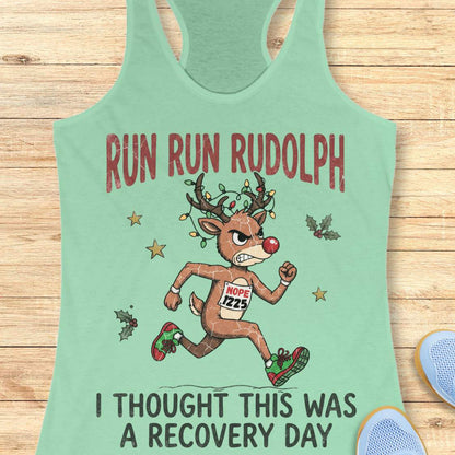 Funny Christmas runner tank top featuring Rudolph the Red-Nosed Reindeer dressed as a runner, sprinting in red and green running shoes with a race bib that reads "NOPE 1225." Rudolph's antlers are wrapped in colorful Christmas lights, and festive holly leaves and stars surround the character. Large distressed text reads, "RUN RUN RUDOLPH" above the illustration and "I THOUGHT THIS WAS A RECOVERY DAY" below. The design is printed on a mint green racerback tank top and combines holiday humor with a relatable 