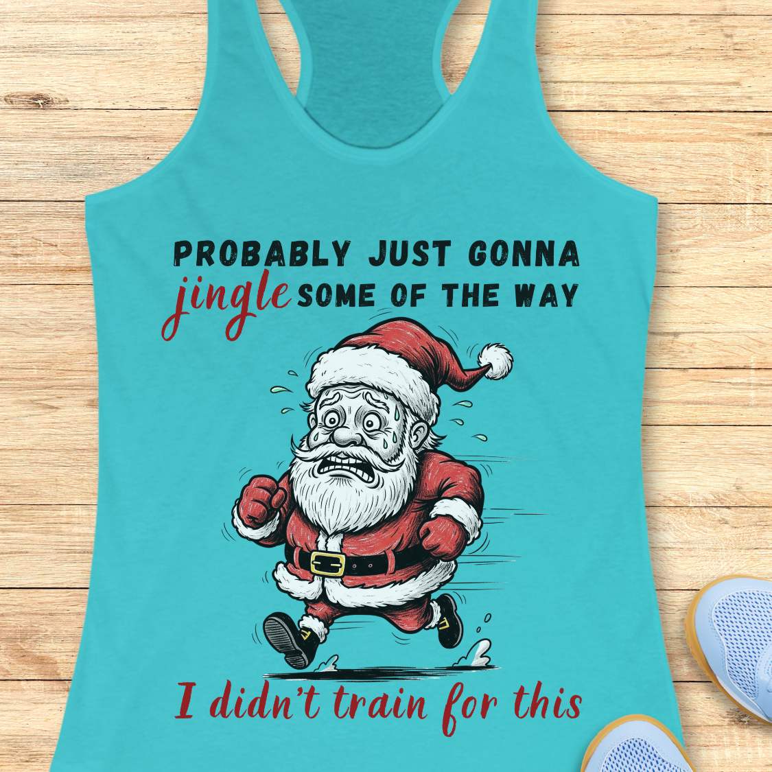 A blue racerback tank top laid flat on a light wood background, featuring a humorous graphic of a running Santa Claus with the text 'PROBABLY JUST GONNA jingle SOME OF THE WAY I didn't train for this'.