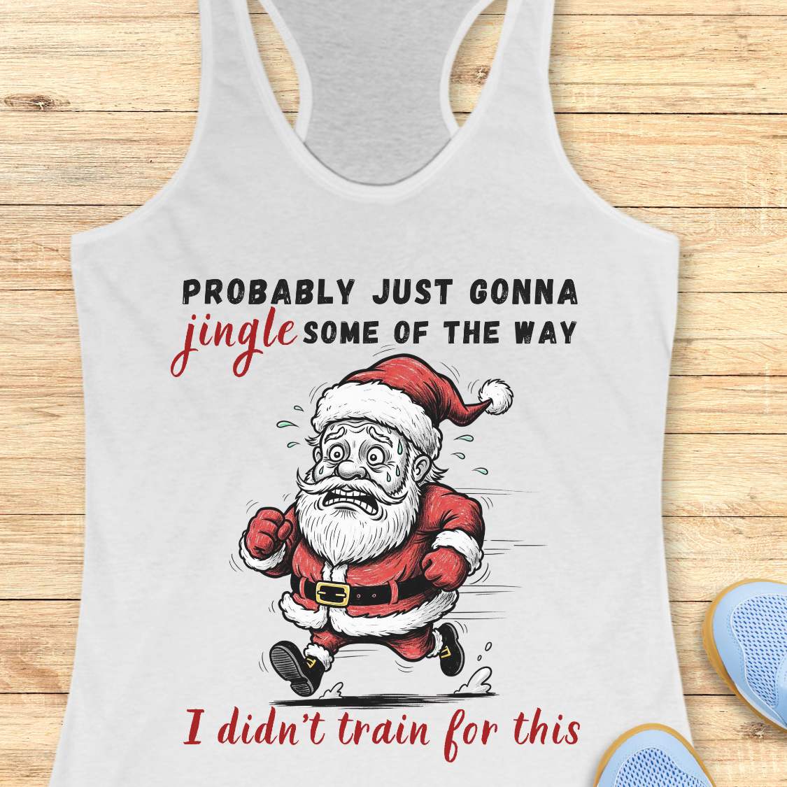 A white racerback tank top laid flat on a light wood background, featuring a humorous graphic of a running Santa Claus with the text 'PROBABLY JUST GONNA jingle SOME OF THE WAY I didn't train for this'.