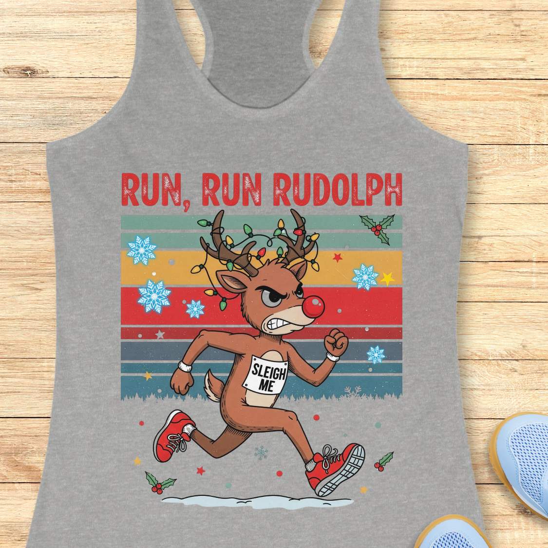 A grey racerback tank top with a colorful 'RUN, RUN RUDOLPH' holiday graphic on the front, shown on a light beige background with decorative text callouts around it.