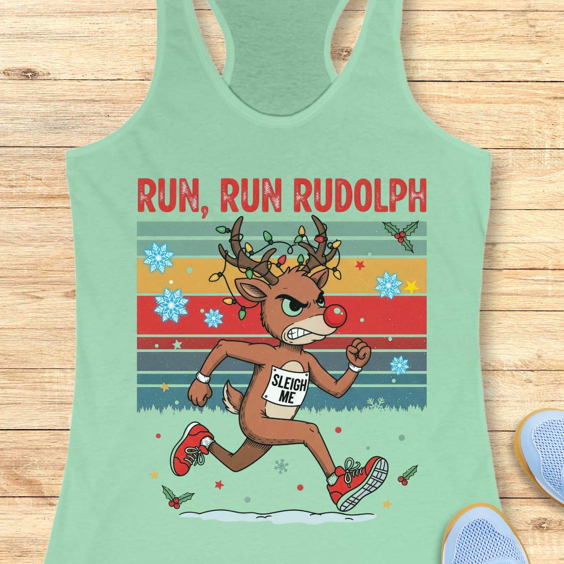 A mint racerback tank top with a colorful 'RUN, RUN RUDOLPH' holiday graphic on the front, shown on a light beige background with decorative text callouts around it.