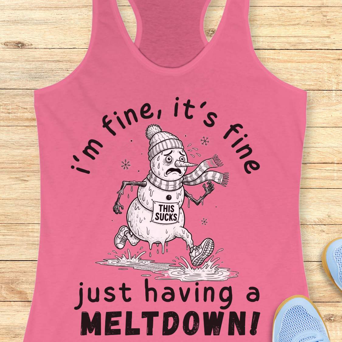 A pink racerback tank top laid flat on a light wood background, featuring a cartoon melting snowman graphic with the text 'i'm fine, it's fine just having a MELTDOWN!'.
