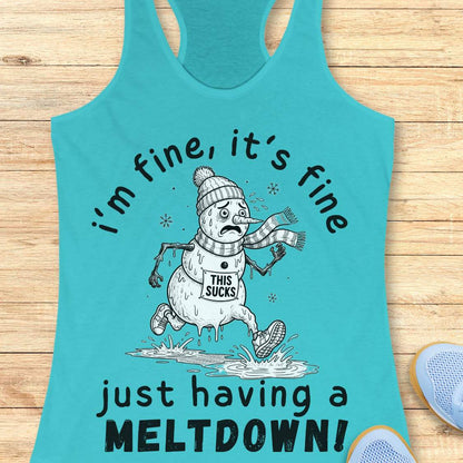 A turquoise racerback tank top laid flat on a light wood surface, featuring a cartoon snowman graphic with the text 'i'm fine, it's fine just having a MELTDOWN!'. A partial blue shoe is visible at the bottom right as a styling prop.