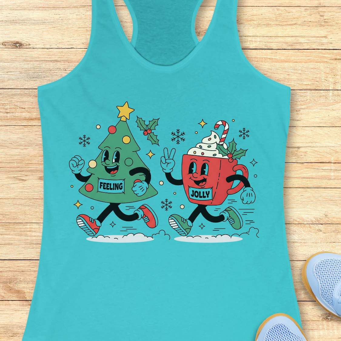 A turquoise racerback tank top laid flat on a light wood surface, featuring a colorful graphic of a green Christmas tree and a red mug with holiday decorations and the words 'FEELING JOLLY'.