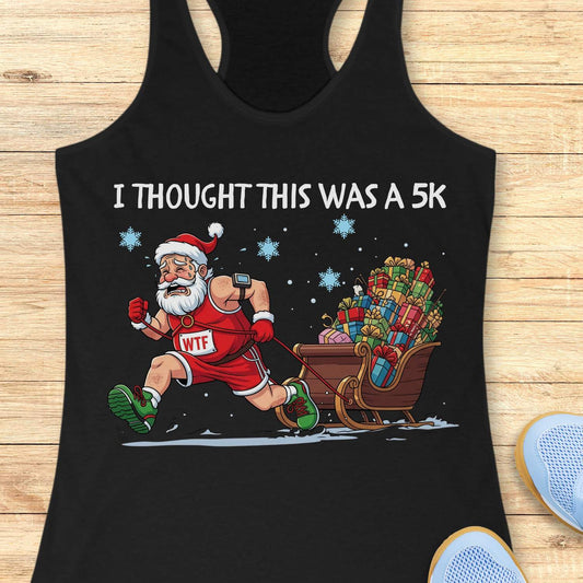 Black racerback tank top displayed on a light wooden surface, featuring a humorous Christmas running graphic. The design shows Santa Claus dressed in a red running outfit, Santa hat, gloves, and green running shoes, pulling a sleigh overflowing with colorful wrapped presents while running through the snow. Santa wears a race bib labeled “WTF,” adding a playful touch to the design. White text above the illustration reads: “I THOUGHT THIS WAS A 5K.” Blue snowflakes and snowy ground details complete the festiv