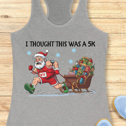 grey racerback tank top displayed on a light wooden surface, featuring a humorous Christmas running graphic. The design shows Santa Claus dressed in a red running outfit, Santa hat, gloves, and green running shoes, pulling a sleigh overflowing with colorful wrapped presents while running through the snow. Santa wears a race bib labeled “WTF,” adding a playful touch to the design. White text above the illustration reads: “I THOUGHT THIS WAS A 5K.” Blue snowflakes and snowy ground details complete the festiv