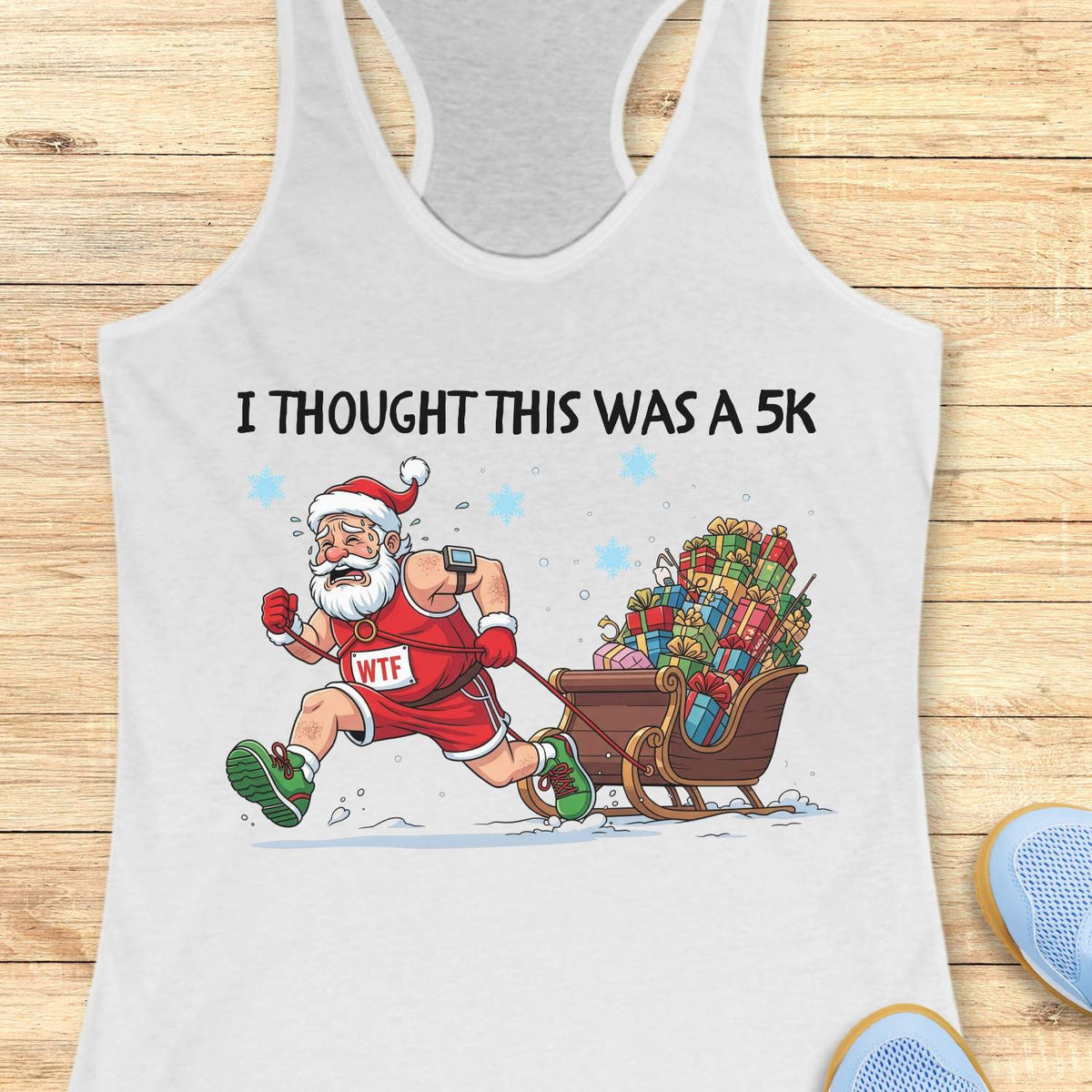 white racerback tank top displayed on a light wooden surface, featuring a humorous Christmas running graphic. The design shows Santa Claus dressed in a red running outfit, Santa hat, gloves, and green running shoes, pulling a sleigh overflowing with colorful wrapped presents while running through the snow. Santa wears a race bib labeled “WTF,” adding a playful touch to the design. White text above the illustration reads: “I THOUGHT THIS WAS A 5K.” Blue snowflakes and snowy ground details complete the festiv