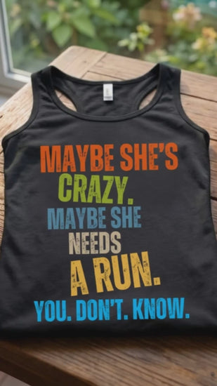 A video with a Black women runner tank top with a funny colorful text 'Maybe she's crazy. Maybe she needs a run. you. don't. know.', on a wooden surface
