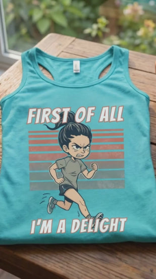 A video of a women runner turquoise tank top laid flat on a wooden table, featuring a cartoon running man graphic with the text 'FIRST OF ALL I'M A DELIGHT'. A ceramic mug of coffee and a small potted succulent sit beside it, with a window and garden visible in the background.